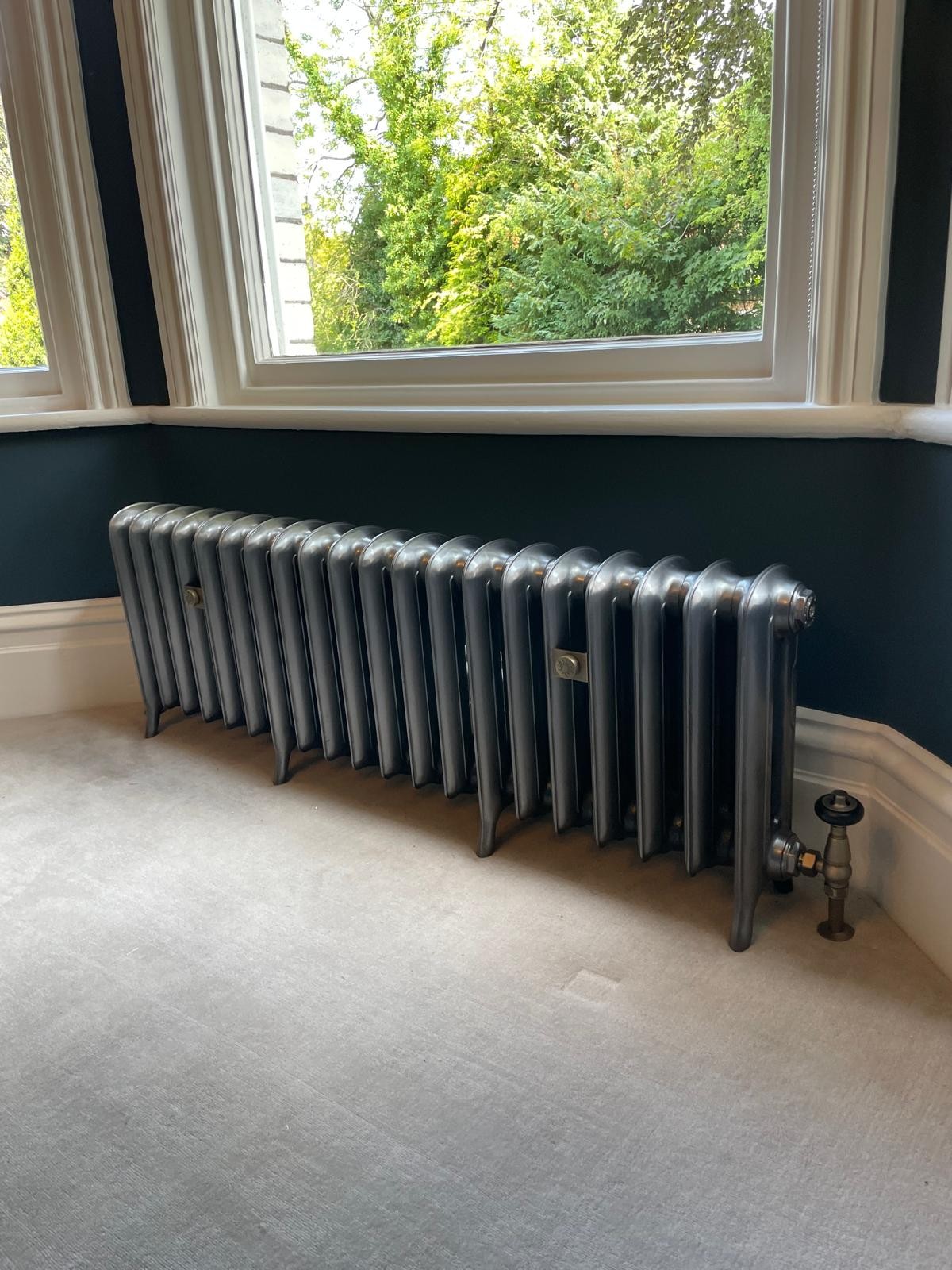 Metallic silver cast iron radiator installed with period valves in a Manchester home